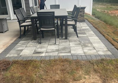 Outdoor patio with a table and chairs; a person stands near the house beside a white fence and grassy yard.