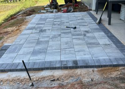 Patio under construction with gray pavers beside a house, tools and materials scattered around.
