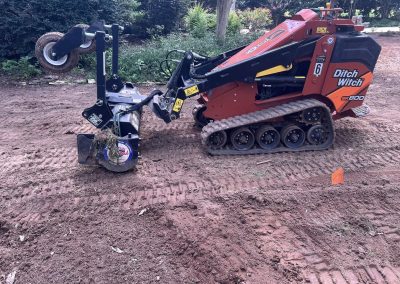 A red Ditch Witch mini skid steer loader with a trencher attachment on a dirt surface.