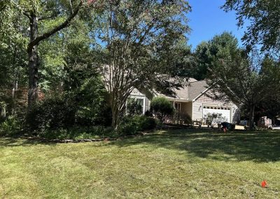 Single-story house with a garage, surrounded by trees and a grassy yard on a sunny day.