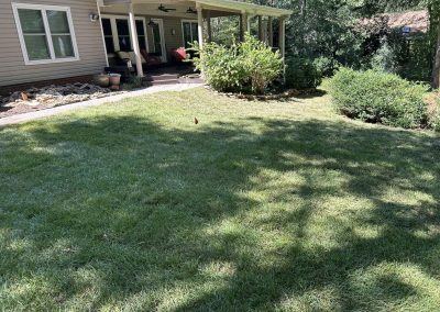A green lawn with shaded areas in front of a house with a covered patio and outdoor seating.