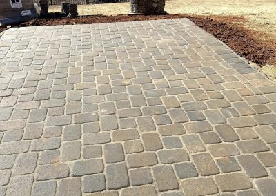A paved patio with stone tiles, overlooking a river and fenced yard with trees in the background.
