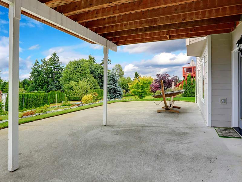 A vacant, modern, beige commercial building with large windows sits on a street corner under a partly cloudy sky, surrounded by palm trees and landscaping.